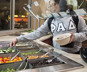 A student grabbing cucumbers for their bowl at the salad bar