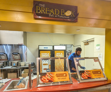 An associate creating sandwiches under the Bread Box logo awning