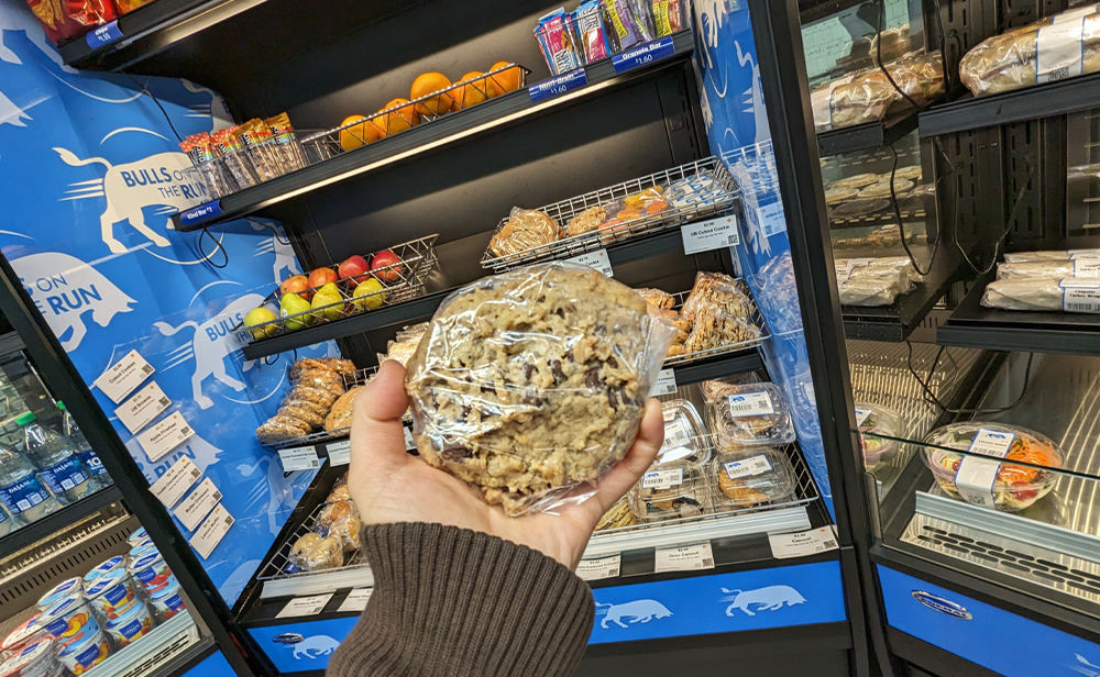 Grabbing an oatmeal raisin cookie, with other bakery items and fruits on the shelves in the background