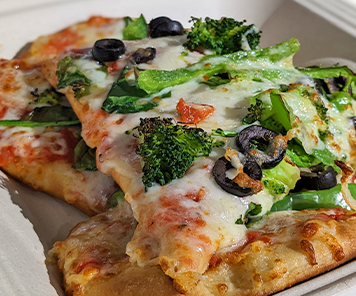 Flatbread pizza consisting of spinach, broccoli, green peppers, and black olives