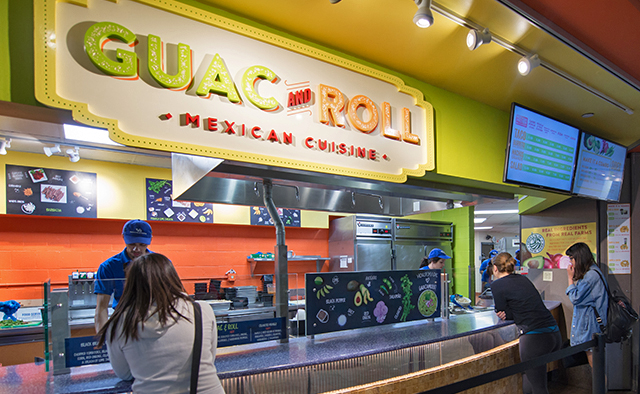 Customers ordering from the Guac & Roll counter under the large logo sign and digital menuboards