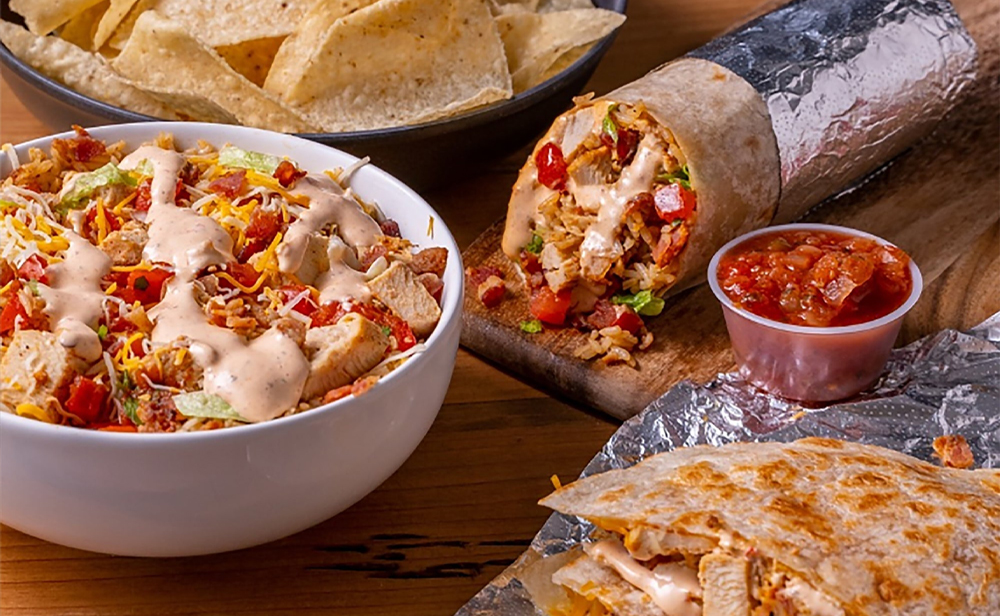 A Moe's burrito, burrito bowl, and quesadilla all with chicken, as well as nachos and a side of salsa.