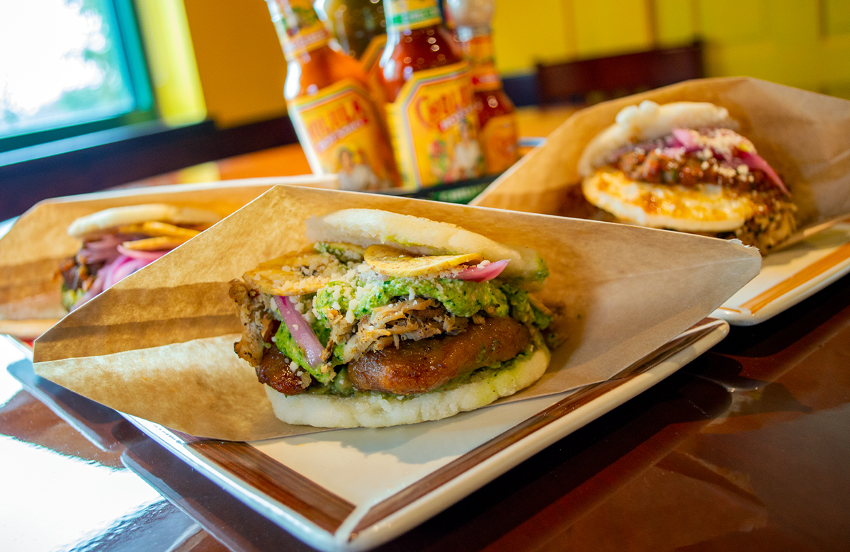 Three arepas plated together with hot sauces behind them