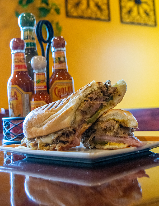 Cuban Sandwich at Sabor Latino plated with hot sauces behind it.