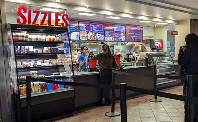 Student ordering from the Sizzles counter overlooking the digital menuboards