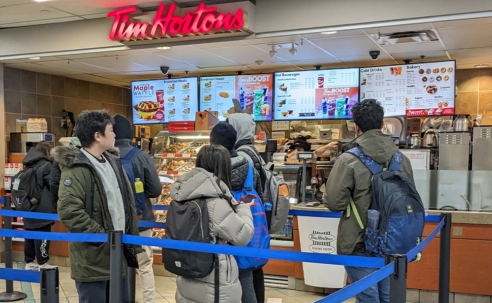 Students lining up to order from the Tim Hortons counter; digital menuboards behind the associates