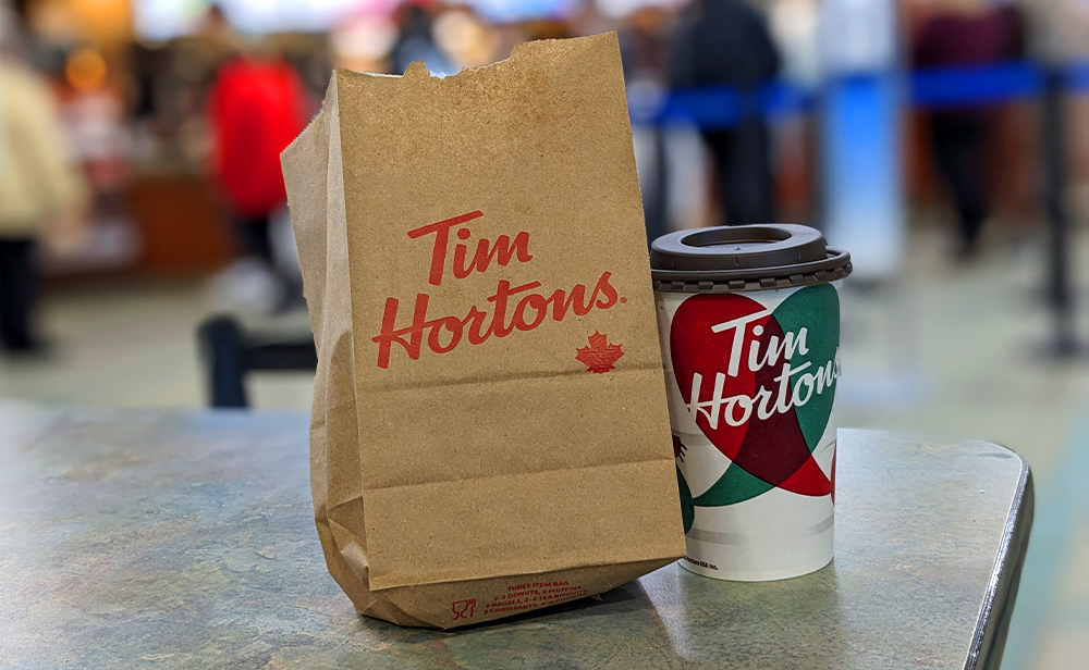 Tim Hortons paper bag and hot coffee on a table with the queue behind them