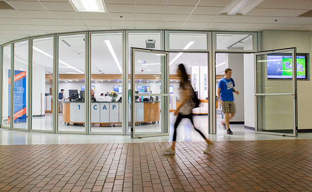Students walking outside of the windowed 1Capen entrance, with a view of an associate at the front desk