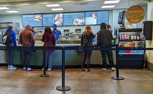 Students in line ordering from Wrap it Up; digital menuboards in the back behind the associates