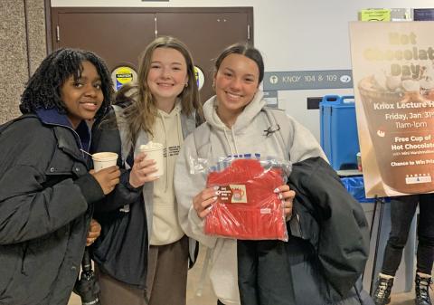 Three students holding hot chocolate and one holds a Coca Cola prize.