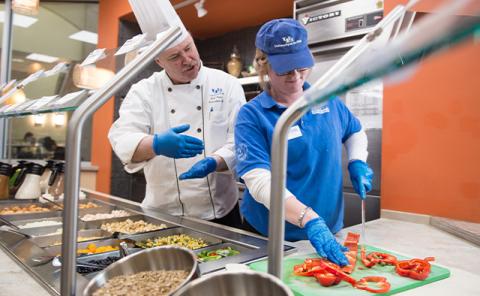 Chef Neal Plazio teaching an associate how to cut peppers in The Bowl