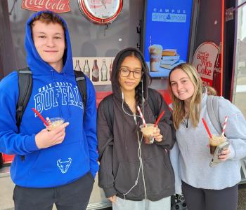 Three students with their Coca Cola floats outside of the Coca Cola Throwback car