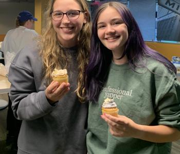Two students smiling and showing their decorated cupcakes