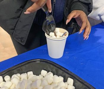 Student scooping marshmallows onto their hot chocolate.