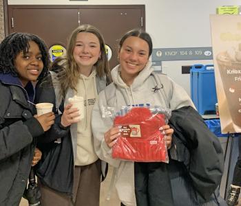 Three students holding hot chocolate and one holds a Coca Cola prize.