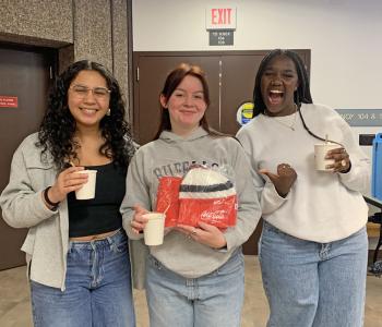 Three students holding hot chocolate and one holds a Coca Cola prize.