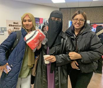 Three students holding hot chocolate and one holds a Coca Cola prize.