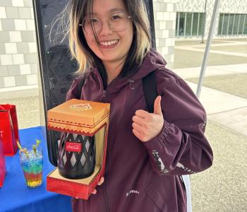 Student smiling showing off their Coca Cola prize and giving a thumbs up