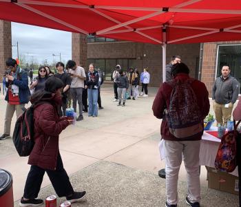 Line forming at the Have a Coke Day table, view from the table showing the Coca Cola cans given out and a student is walking away with her prize