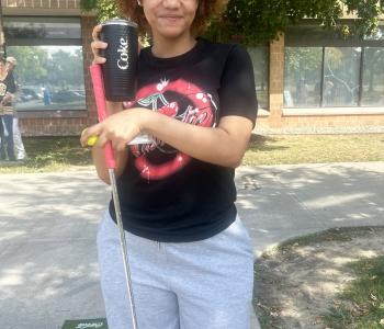 Student posing with a golf club and her prize of a Coca Cola cup