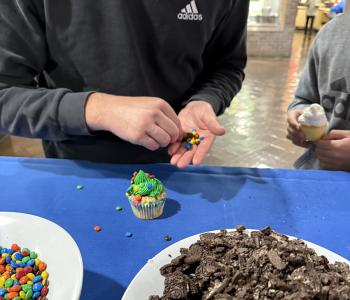 Student decorating their frosted cupcake with topings