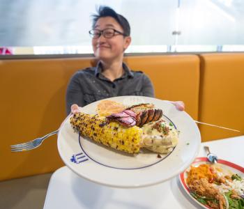 A student holding out a plate of lobster tail, mashed potatoes and corn on the cobb during Lobster Night at C3.