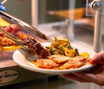 A retrieval of carved meat onto a plate that already has grilled zucchini and ravioli. Photo by Meredith Forrest Kulwicki.