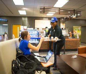 An associate giving a student a free coffee sample at Whispers Café. Photo by Douglas Levere.