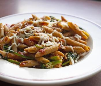 Penne pasta with red sauce, broccoli and spinach, topped with parmesan cheese.