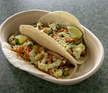 Two chicken tacos topped with tomato, cheese, cilantro, lime wedge and a green sauce.