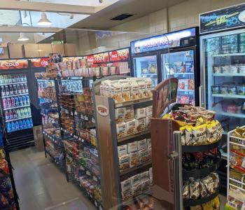 Inside Main Street Store, where chips, cookies, and snacks line the shelves. Coca-Cola products are in the large cooler in the back and frozen foods are at the right wall.