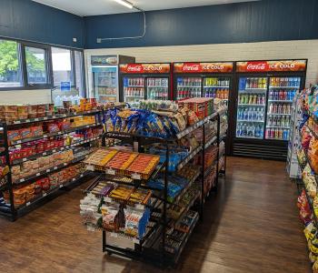 Shelves lined with snacks, and Coca-Cola coolers lined with drinks, in the back at Teddy's convenience store in Governors.