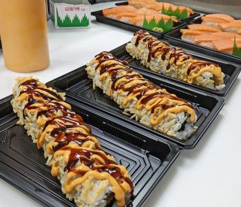 Sushi rolls being made topped with crunchy tempura flakes, spicy mayo and soy sauce.