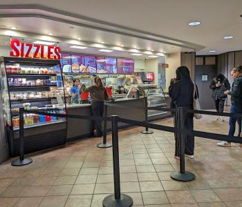 A student ordering at the Sizzles counter and other students lining up.