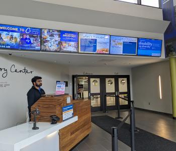 The lobby of C3 with digital sign menus on TVs above the doors. An associate is prepared to swipe UB Cards.
