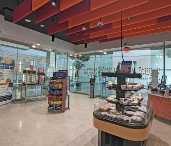 The interior of Corner Café at JSMBS. You can see some grab & go items, a snack shelf, a breakfast sandwich warmer, and one of the ordering kiosks.