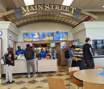 Students in line to order from Main Street Market at the same location as Goodyear Dining Center, with the digital menuboard signs behind the associates.