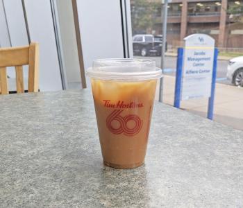 A cup of iced coffee at Tim Hortons in Alfiero Center, with the Alfiero sign outside in the background.
