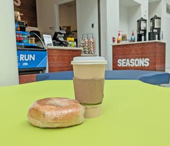 A bagel and self serve hot coffee on the couch in front of Seasons at Center for the Arts.