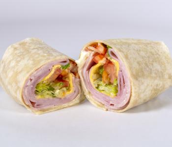 A ham wrap with tomatoes, lettuce and cheese on a white tortilla.