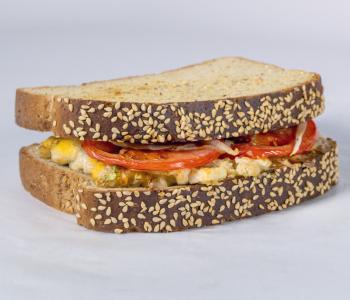 A deli breakfast sandwich with scrambled eggs, tomato, onion, lettuce, and cheese.