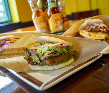 A trio of arepas, the front one in focus, with the hot sauce center piece on the table in the background.