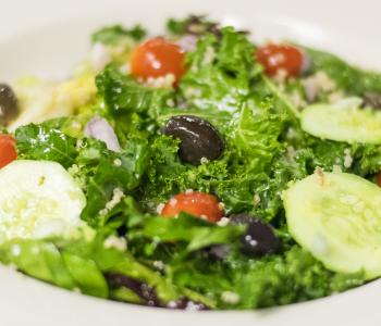 A closeup of the Power Greek signature salad: kale, cucumbers, kalamata olives, grape tomatoes, quinoa, diced onions, chickpeas and feta.